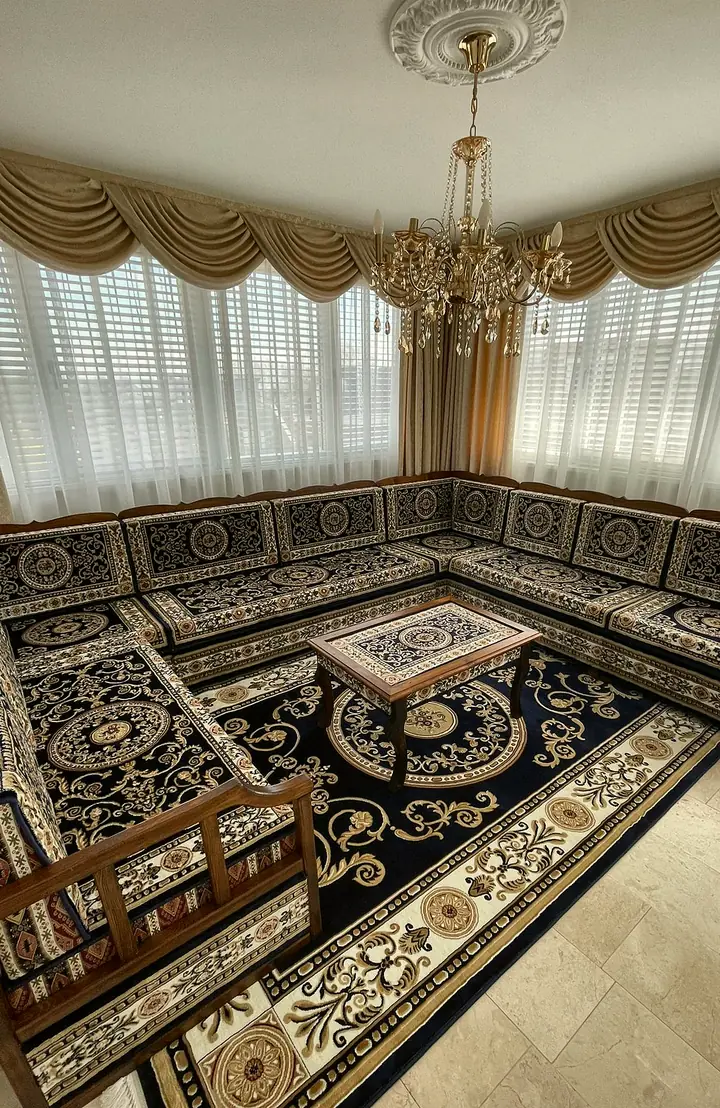 Navy and cream carpet cushions on wooden sedir benches running around three walls, with a matching medallion rug below sheer curtains