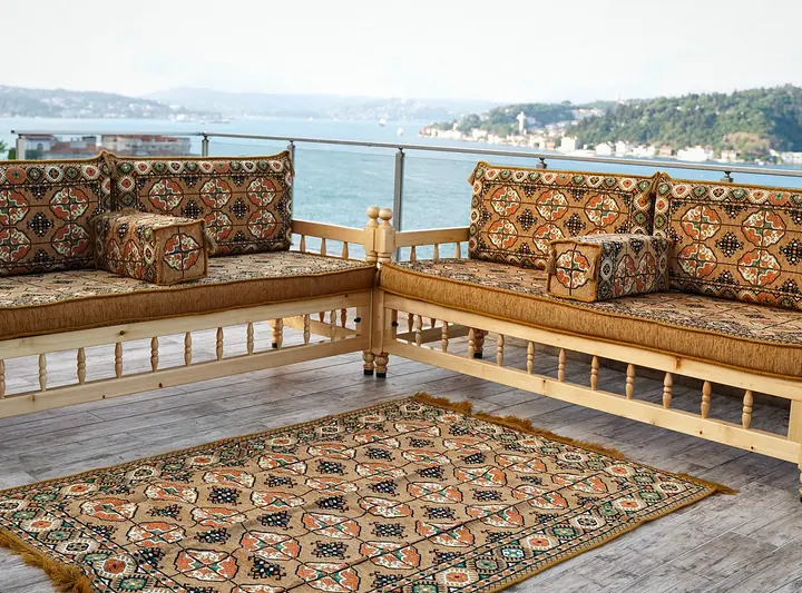 Two wooden benches meeting in an L with gold gul cushions and armrest bolsters, a patterned rug in the corner