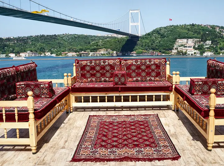 Maroon gul-pattern cushions with cream and black octagons on wooden benches arranged in a U around a rug