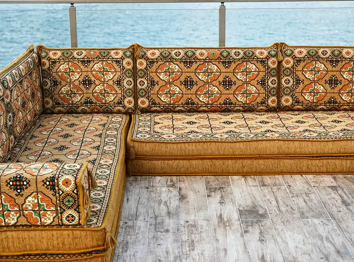 Corner of a gold Afghan Gul floor couch, showing the short corner backrest and a square box armrest in the foreground