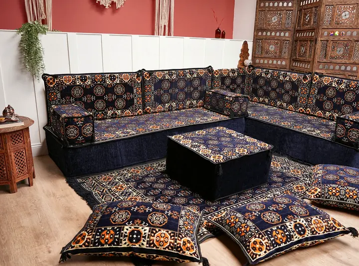 Navy blue corner floor seating with a dark ottoman and floor cushions in a room with a pink wall and carved screens