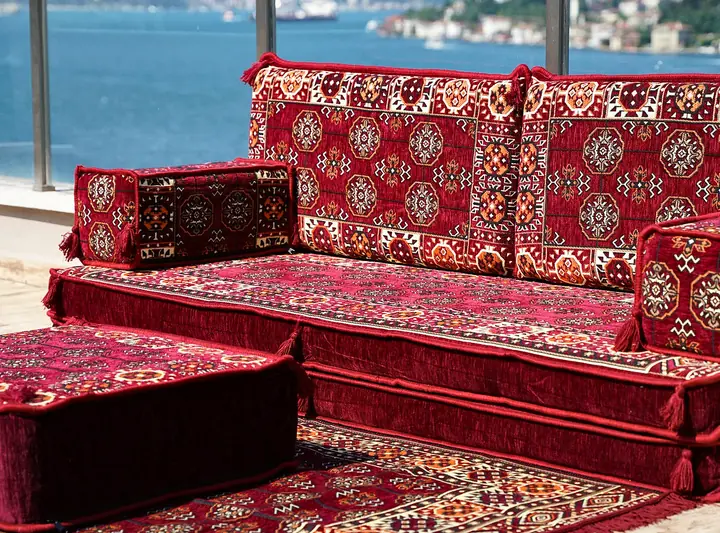 Close view of a thicker maroon gul seat cushion beside its ottoman, with the plain band around the base of the seat