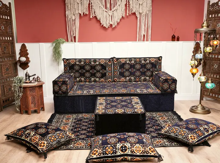 Navy blue gul-pattern floor couch with an ottoman and floor cushions against a pink wall with macrame, beside a mosaic lamp stand