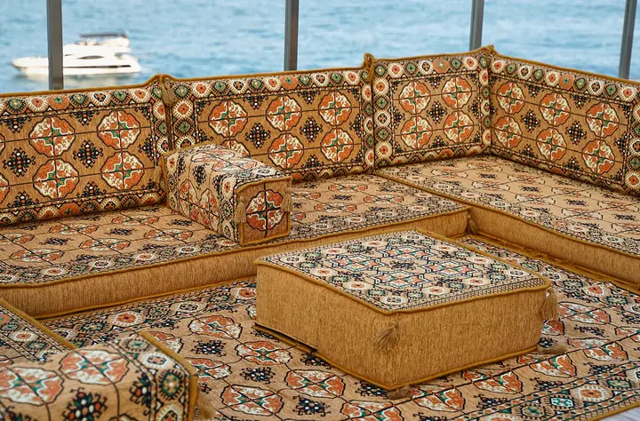 View from inside a gold U of floor seating, looking past the ottoman on its patterned rug to the back run of seats
