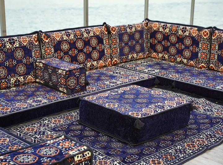 Angled view of navy blue three-sided floor seating with an ottoman and a rug filling the open space between the runs