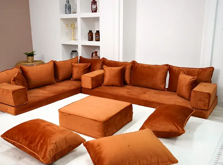 Amber orange velvet corner floor sofa with an ottoman and floor pillows in a white living room