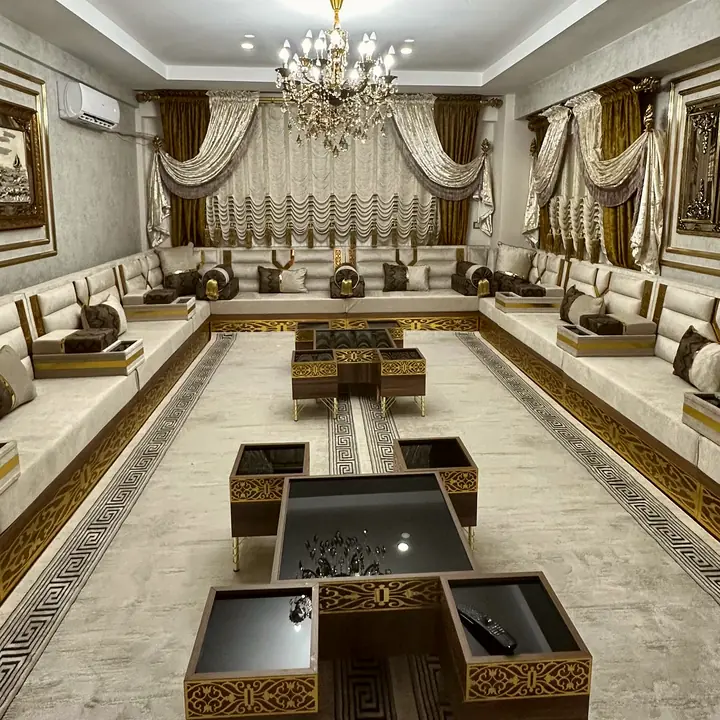 Cream majlis lining both sides of a long room, with gold-trimmed bases, black glass-top tables and a crystal chandelier
