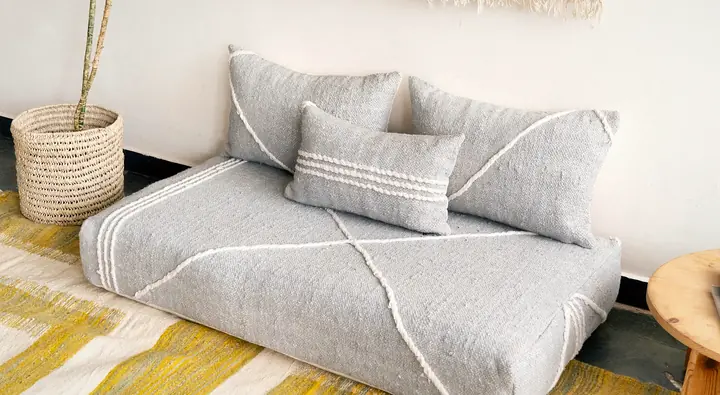 Angled view of a light gray floor couch with a white line pattern and its back pillows on a yellow rug