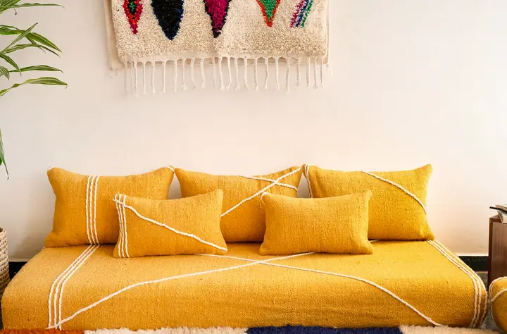 Mustard yellow cotton floor couch seen from the front, with lumbar pillows lined up under a wool wall hanging