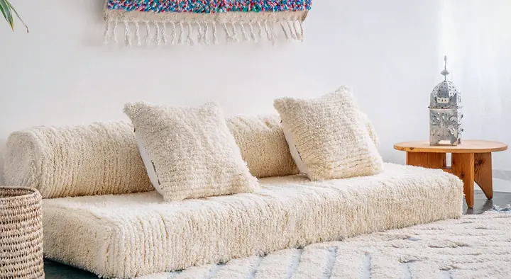 Angled view of a cream floor couch with its round bolster and pillows, and a lantern on a wooden side table