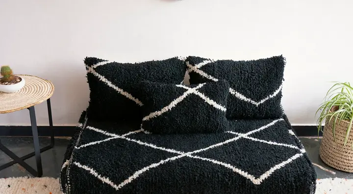 Black shag floor couch with white lines, centered between a small side table and two potted plants