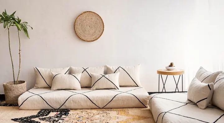 Wide view of cream flatweave floor couches with black lines set along two walls on a vintage rug