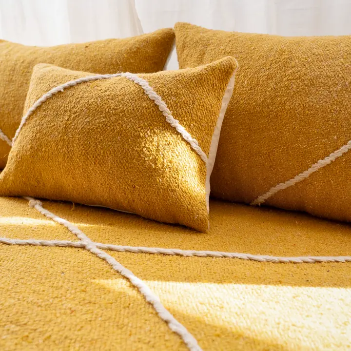 Close view of mustard yellow woven cushions with white cord stitching running along the seams