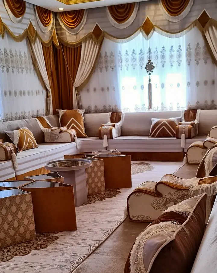 Beige and amber majlis in a long room with fringed swag valances, embroidered sheers, star-shaped mirrored tables and a patterned rug
