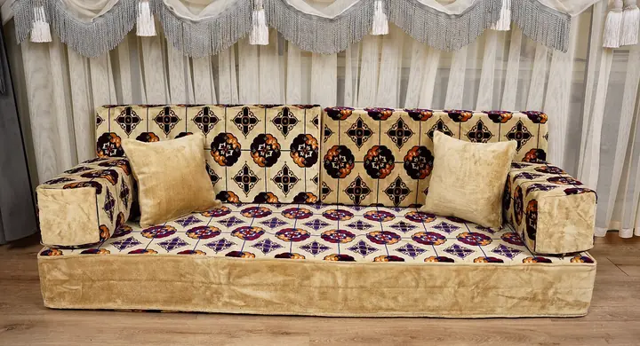 Beige floor sofa with cream covers carrying plum and orange medallions, two upright backrests and matching arms on a white background