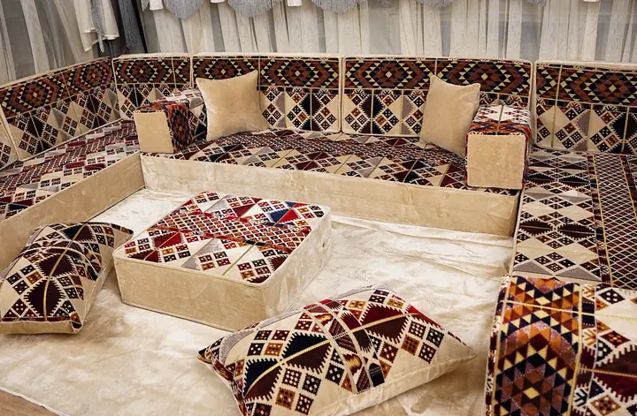 Geometric patterned backs and side panels surround plain beige seats, with a matching ottoman and floor pillows