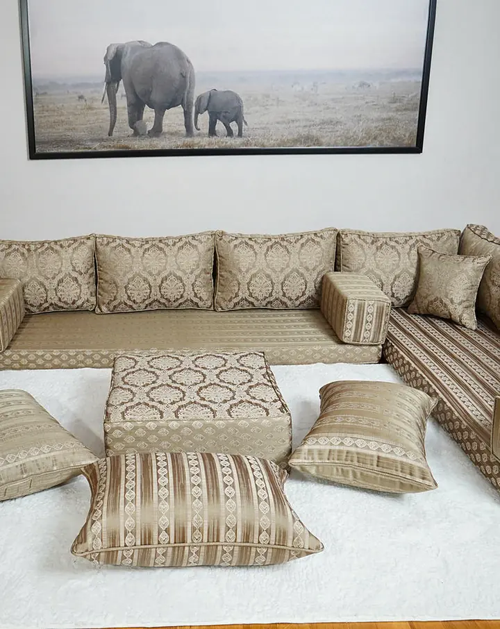 Beige and gold damask U-shaped floor sofa set with a square ottoman and floor pillows on a white shag rug in a living room