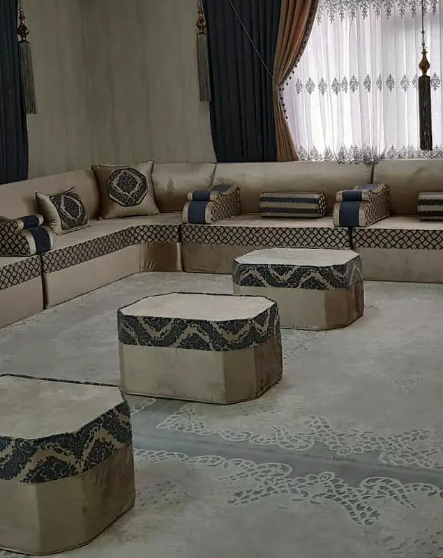 Beige velvet U-shaped majlis with navy wave-pattern bands running under two wide curtained windows, three cut-corner poufs in the middle