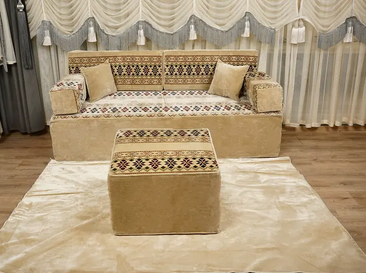 Beige velvet floor sofa with star-pattern backrests and armrests, two plain pillows and a matching square ottoman on a cream rug
