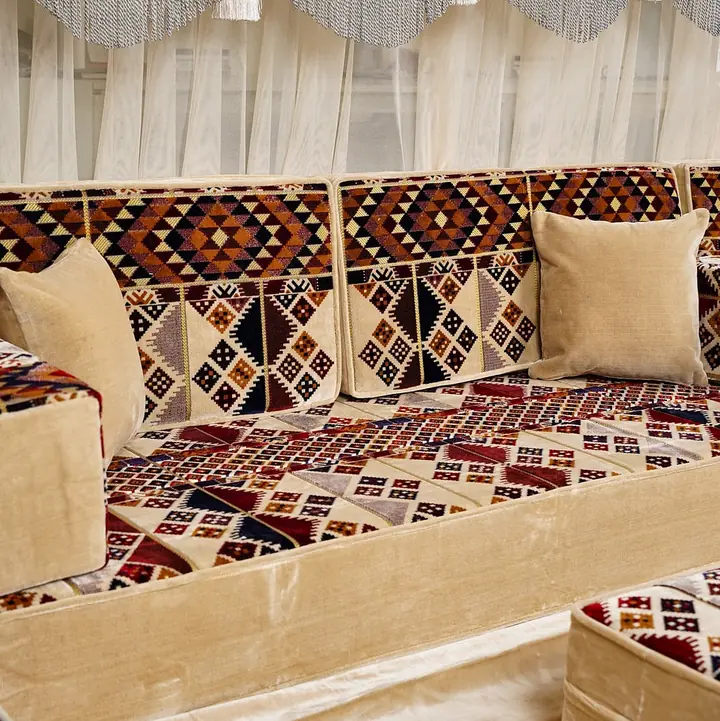 Close view of a beige velvet floor seat with kilim-diamond backrests, a square armrest bolster and two plain cream pillows by sheer curtains