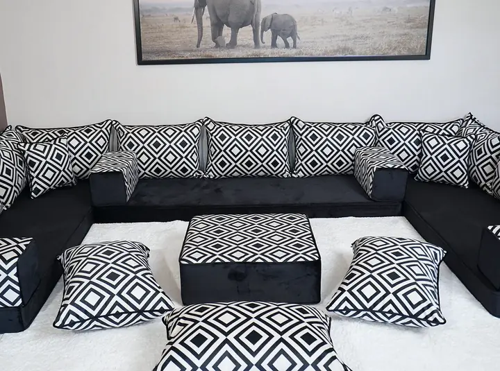 Black floor seats enclose a white rug on three sides, with patterned bolsters between the seats and a square ottoman in front