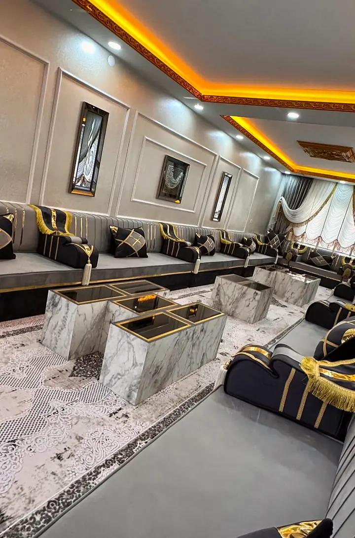 Sculpted black armrest with gold fringe ending a gray run, facing cube tables on a white and gray patterned rug
