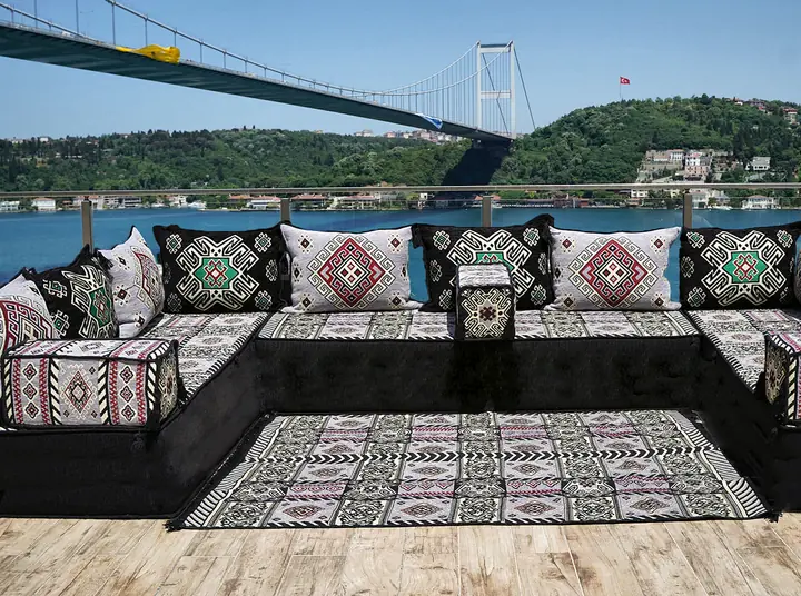 Black and light gray kilim U-shaped majlis around a kilim rug on a terrace below a suspension bridge