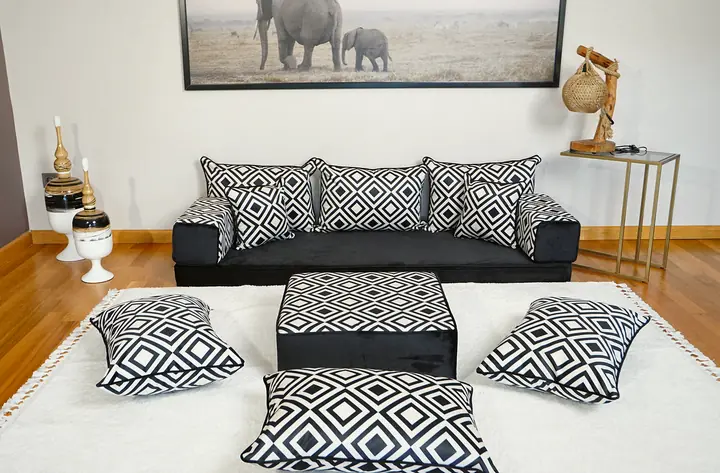 Black straight seating and a square ottoman share white lattice covers, with loose cushions beneath an elephant wall print