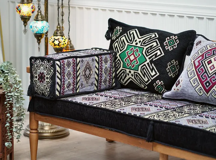 Black and lilac kilim-pattern bench sofa with a bolster and two pillows, a mosaic floor lamp and a carved side table with trailing greenery