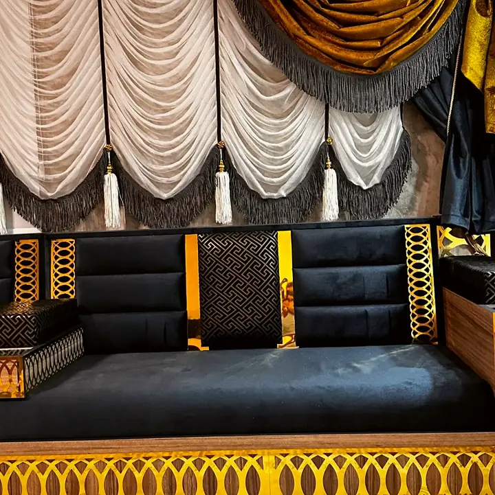 Channel-stitched black backrests with gold panels and a patterned square pillow above a bright gold oval-lattice base