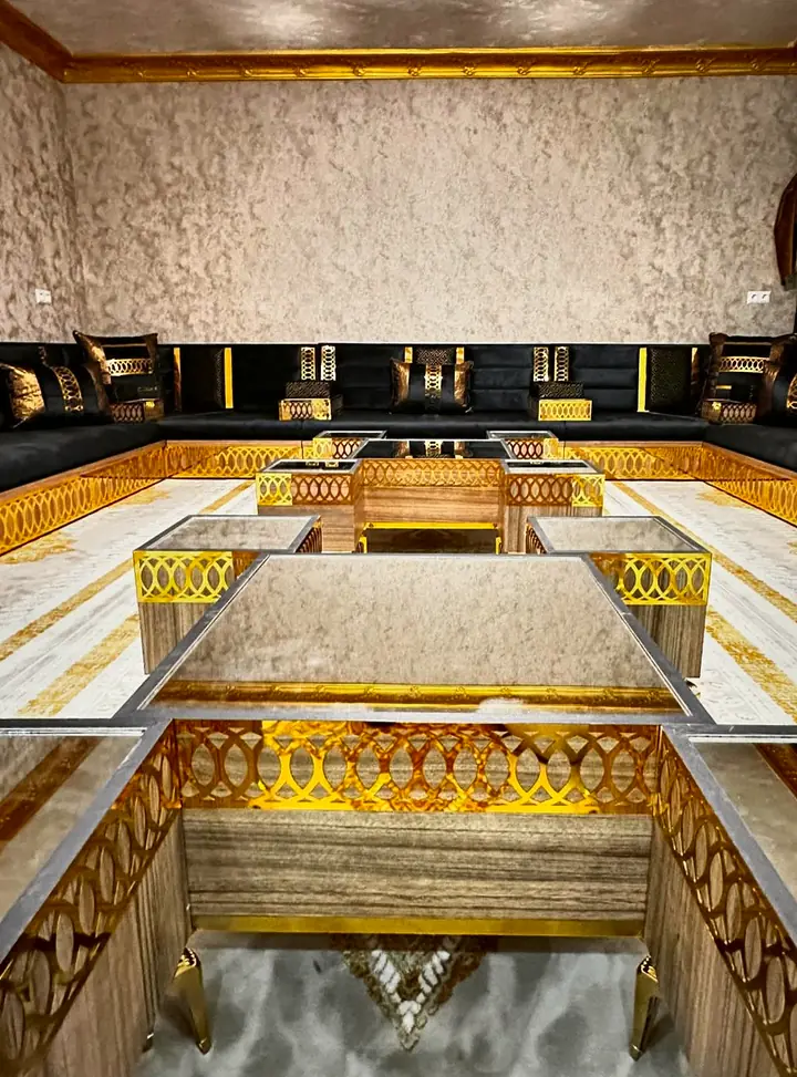 Wood and glass nesting tables with gold oval-lattice panels in front of black velvet seating on a matching gold base