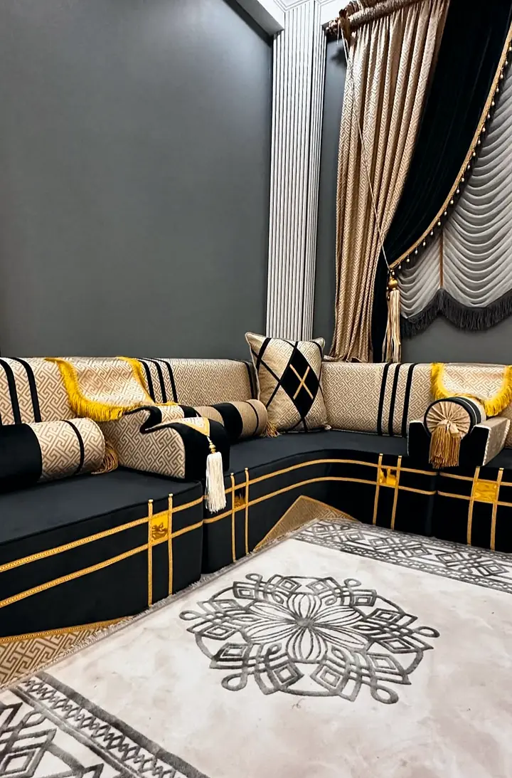 Corner of a black velvet floor majlis with gold-banded seats, sand Greek-key backrests and an ivory knot-pattern rug