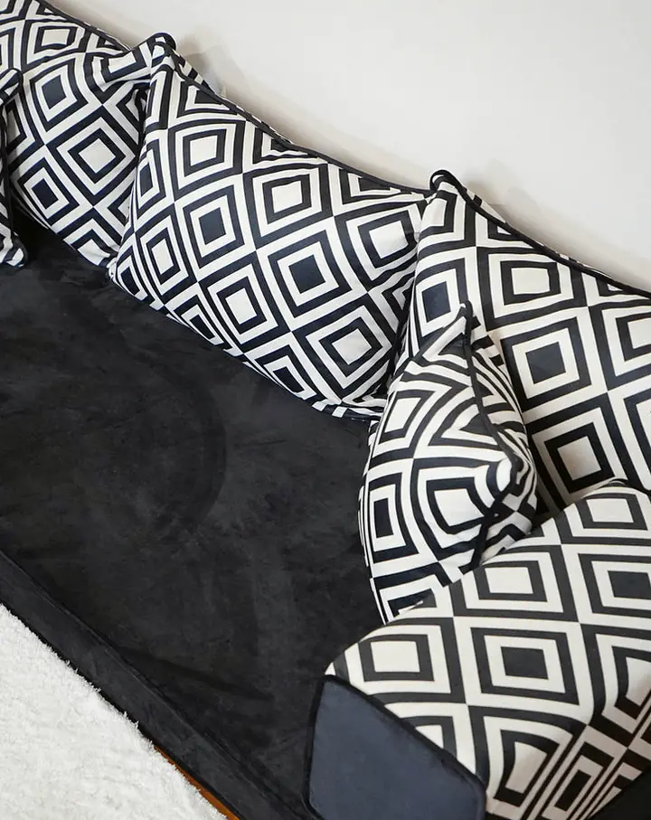 High-angle view of a black velvet floor seating set with black-and-white diamond-print backrests and pillows beside a white shag rug