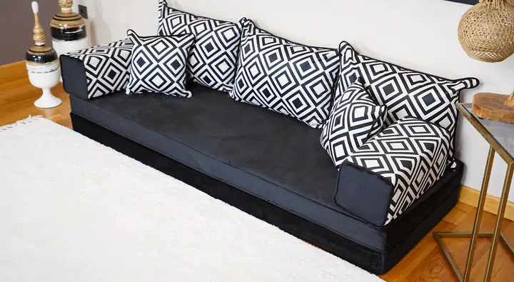 Black velvet floor sofa against a white wall with black-and-white diamond-print backrests and bolsters, beside a rope lamp on a brass table