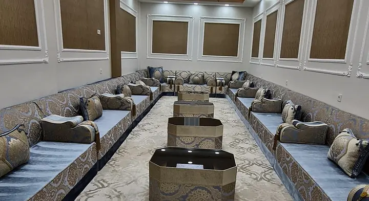 Blue-grey velvet seats with gold jacquard backrests along both walls of a long panelled hall, octagonal tables down the middle