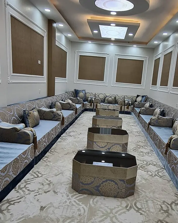Blue-grey velvet seats with gold jacquard backrests along both walls of a long panelled hall, octagonal tables down the middle