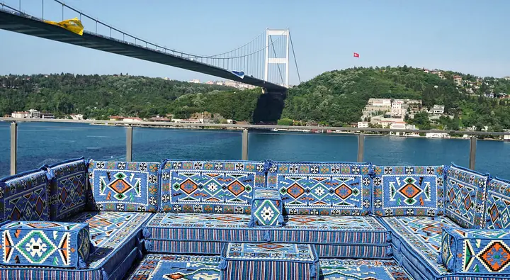 Royal blue kilim-pattern U-shaped majlis floor sofa with a matching rug and a low ottoman, arranged on an open-air terrace