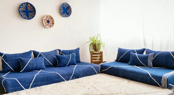 Royal blue Moroccan floor seating turning a corner in an L-shape, with a white line pattern and pillows over a cream shag rug