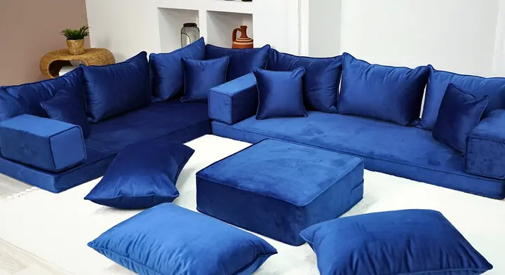 Royal blue velvet corner set with square backrests and small throw pillows, a blue ottoman and floor pillows in front