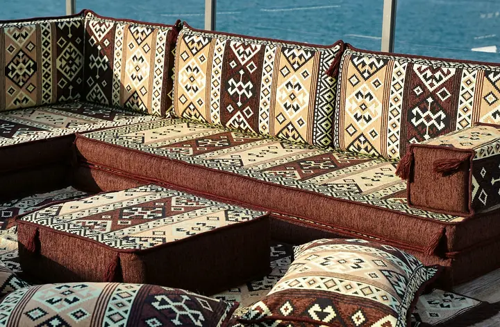 Close view of brown and cream kilim-weave floor seating with thick seats, tasseled backrests, a low ottoman and scattered floor pillows