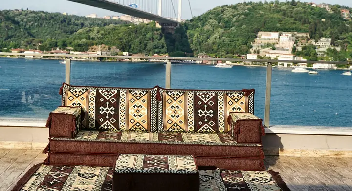 Single brown and cream kilim floor sofa set on a terrace: a two-layer seat, two backrests, two armrests, an ottoman and a fringed rug