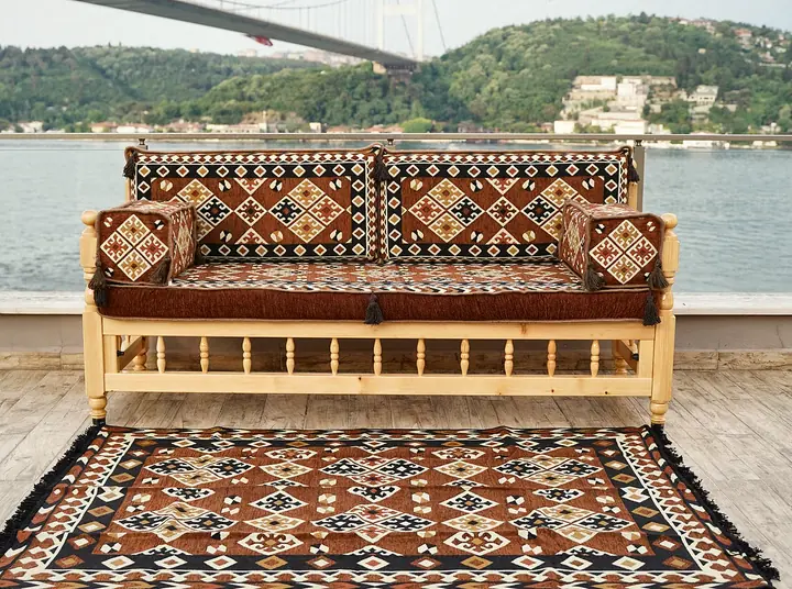 Single sedir bench with brown diamond kilim seat and back cushions, two armrest bolsters and a fringed kilim rug in front