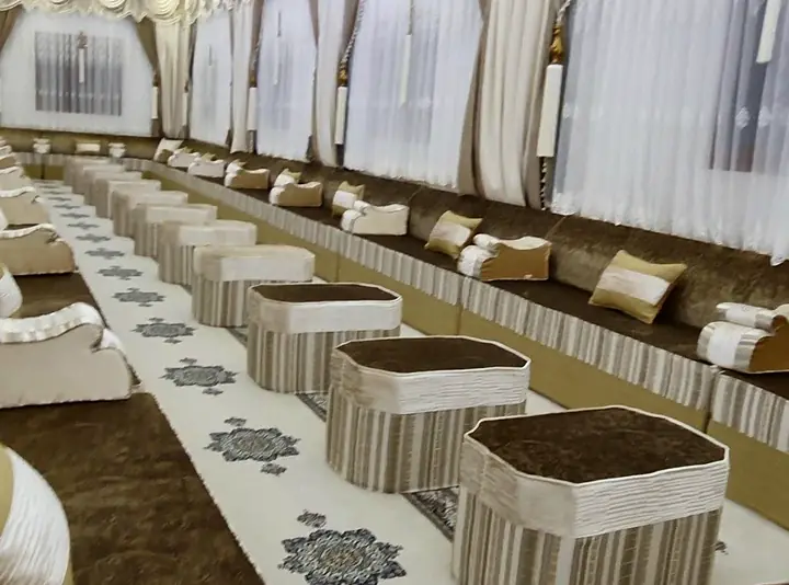 Long hall lined with brown crushed-velvet floor seating, cream backrest pillows and striped octagonal ottomans down the middle