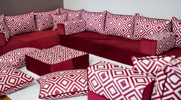 Burgundy velvet floor seating with red and white diamond-print backrests, loose floor pillows and a matching ottoman on a pale rug