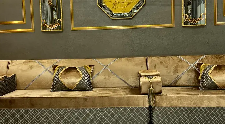 Camel velvet floor majlis running along a single wall, with diamond-pattern pillows, a quilted grey base and gold-framed panels above