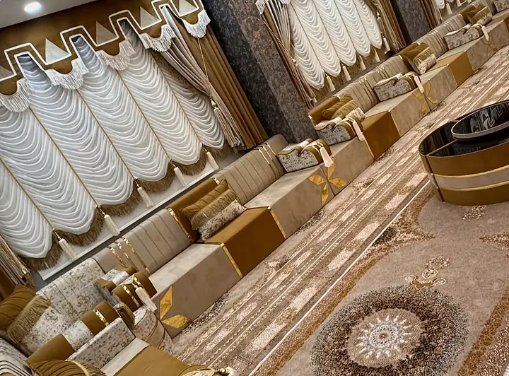 Cream and caramel seats with gold trim surround round dark tables on patterned carpet beneath white and brown layered curtains.
