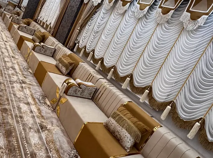 Cream seats with gold bands and caramel panels form a long row beneath white drapes beside a brown patterned carpet.