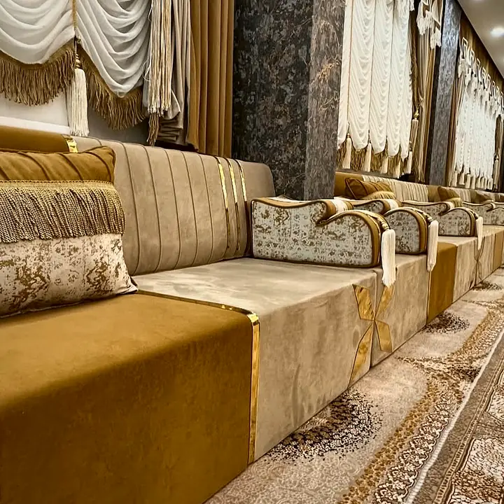 View along a caramel and cream majlis run showing polished gold strips, a fringed lumbar pillow and a channel-stitched backrest