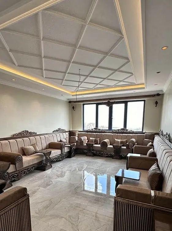 Raised brown majlis seating on carved wooden frames along two walls of a room with a polished marble floor