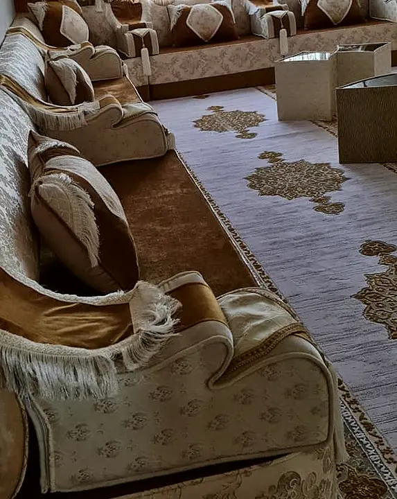 Long narrow room seated in champagne and gold along two walls, with fringed throws over the armrests and glass-topped cube tables